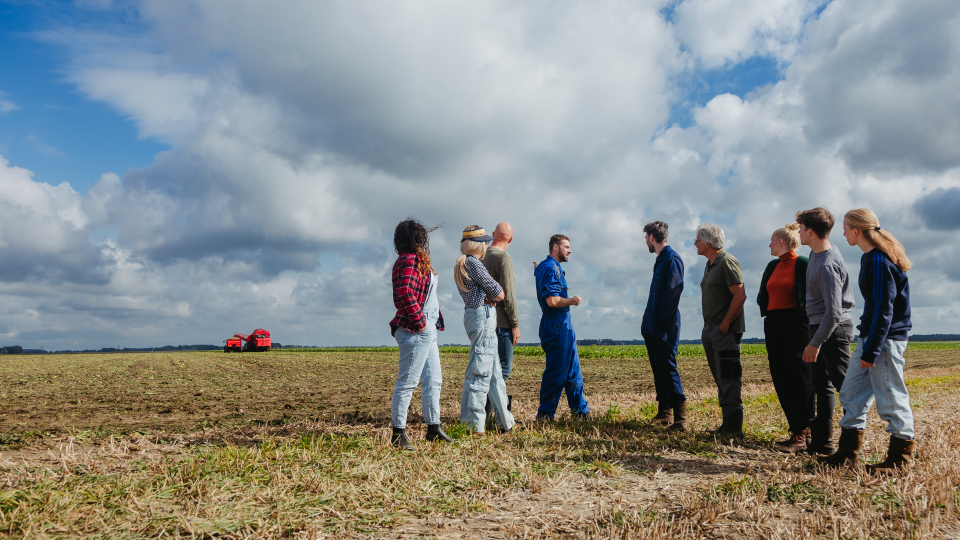 Groep mensen op een geoogst suikerbietenveld praten over plannen voor het gebied